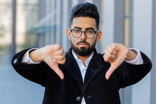 Dislike. Upset Indian businessman showing thumbs down sign gesture, expressing discontent, disapproval, dissatisfied bad work, mistake outdoors. Arabian Hindu freelancer guy in downtown city street