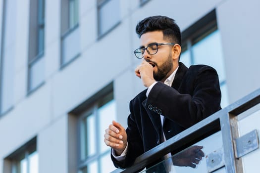 Tired exhausted Indian businessman yawning, sleepy inattentive feeling somnolent lazy bored gaping suffering from lack of sleep, falling asleep outdoors. Arabian Hindu freelancer guy in downtown city