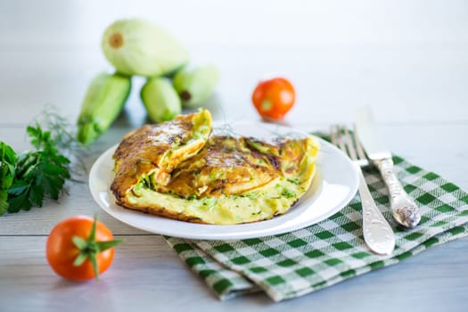 Fried omelet with zucchini,in a plate on a wooden table.