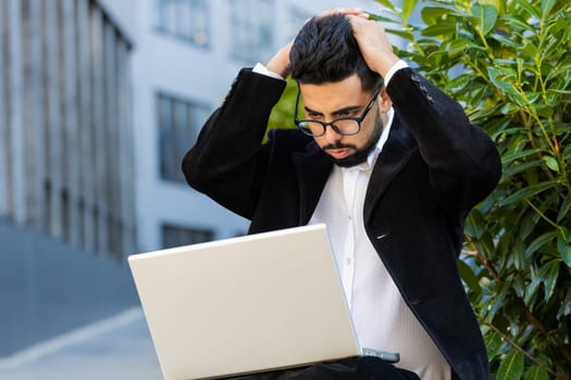 Displeased worried Indian businessman use laptop notebook typing browsing working loses bad news loss database fail computer virus error problem outdoor. Arabian Hindu freelancer executive manager ceo