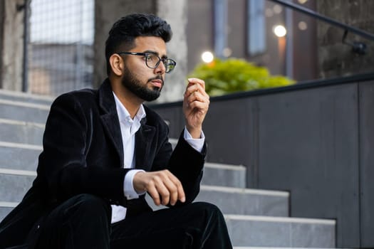 Unhappy sad Indian business man frustrated stress pensive feeling bad after company unemployment lost job problem solution crisis outdoor. Arabian Hindu freelancer guy sitting on stairs downtown city