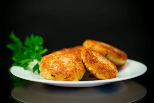 Cooked fried fish cutlets in a plate with herbs, isolated on a black background.