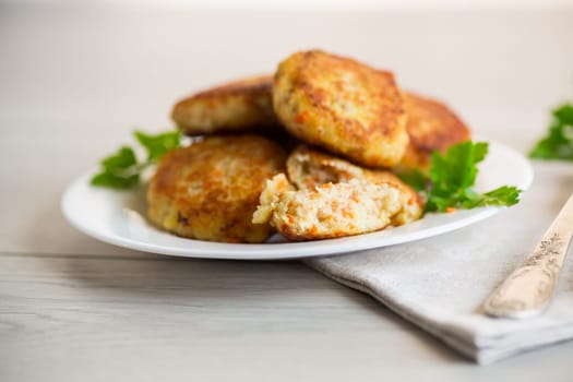 Cooked fried fish cutlets in a plate with herbs, on a light wooden table.