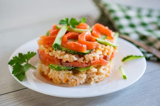 Boiled white rice with salted red fish, cucumbers and other vegetables with herbs in a plate, on a wooden table.