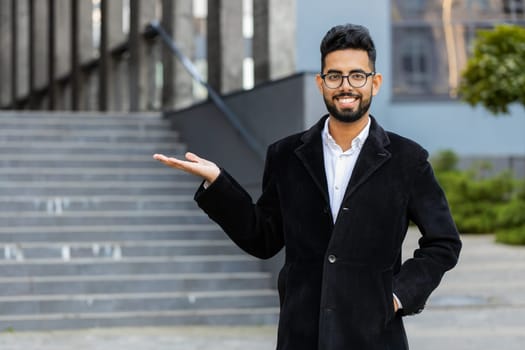 Indian businessman showing pointing empty place advertising area for commercial text copy-space for goods promotion outdoors. Arabian Hindu freelancer guy in downtown city street. Business people