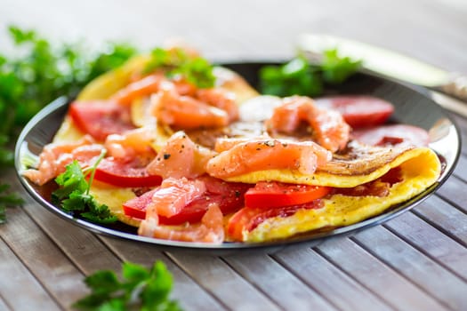 Fried omelette with tomatoes, vegetables and pieces of lightly salted red fish, on a wooden