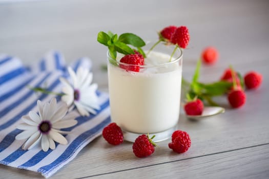 Sweet cooked homemade yogurt with fresh raspberries in a glass, on a light wooden table.