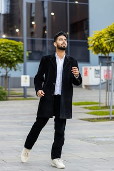 Portrait of happy Indian businessman smiling friendly, glad expression looking forward, feel satisfied good news outdoors. Arabian Hindu freelancer in downtown city street. Business people. Vertical