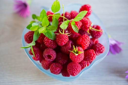 Fresh ripe raspberries in a glass bowl on a light wooden table.
