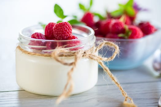 Sweet cooked homemade yogurt with fresh raspberries in a glass jar, on a light wooden table.