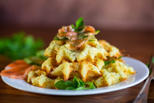 Cooked potato waffles with lightly salted red fish and herbs in a plate, on a wooden table.