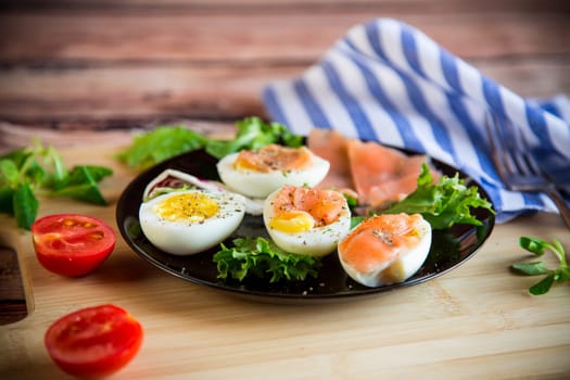 boiled eggs with salted red fish, herbs and seasonings in a plate on a wooden table.