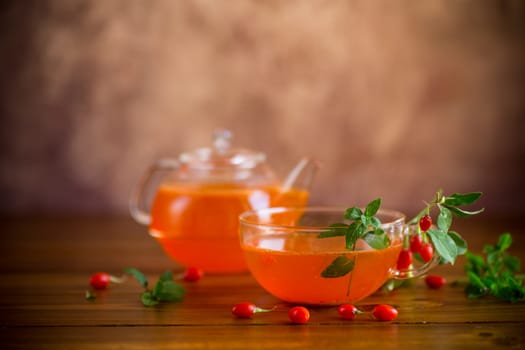 Prepared drink from ripe goji berries in a glass cup and teapot, on a wooden table.