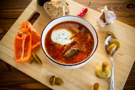 Cooked vegetarian beetroot soup with mushrooms and other vegetables in a bowl with spices, on a wooden table.