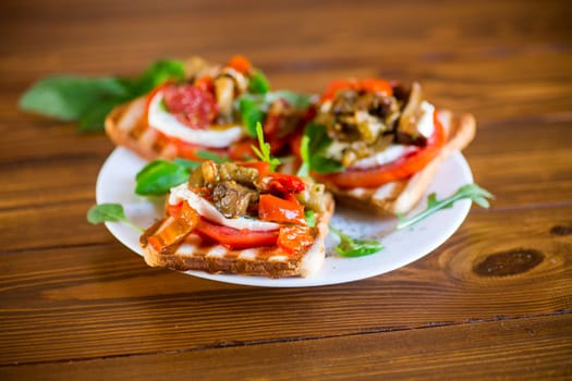 Prepared sandwich with tomatoes, mozzarella and fried eggplant with mushrooms in a plate on a wooden table.