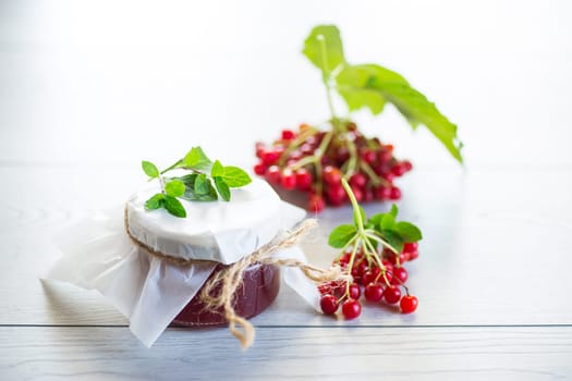 viburnum jam in a glass jar and fresh red viburnum on a light wooden table.