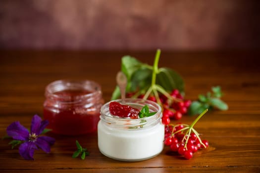 Prepared homemade yogurt with viburnum jam and viburnum on a wooden table.