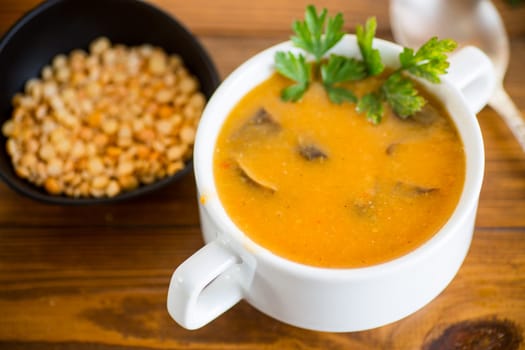 Cooked dried pea puree soup with mushrooms in a bowl on a dark wooden table.