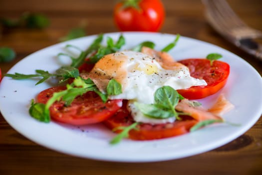 Cooked poached egg with herbs, lightly salted salmon and tomatoes with spices on a wooden table.