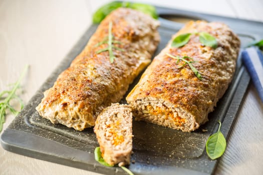 Cooked minced meatloaf with vegetable filling inside, on a wooden table.