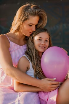 Portrait of mother and daughter in pink dresses with flowing long hair against the black backdrop. The woman hugs and presses the girl to her