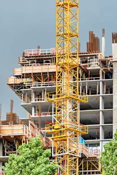 Construction of concrete high rise residential building with yellow crane in front on stormy weather background