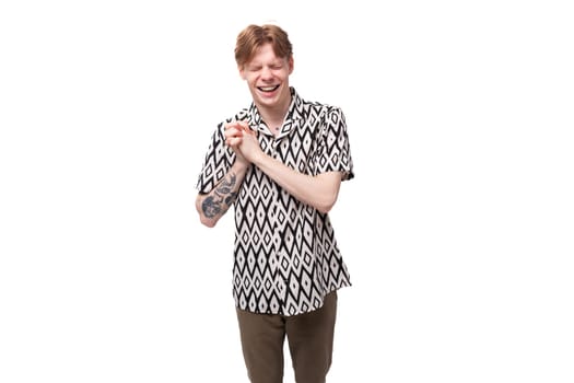 young cheerful handsome red-haired man dressed in a summer shirt with a rhombus print on a studio background.