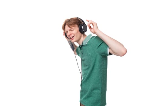 young positive slender student european man with red hair listens to music in headphones with a wire.