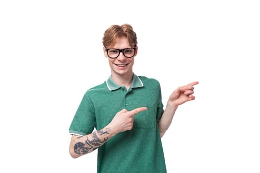 young smart caucasian man with red hair dressed in a green t-shirt points his hand to the side.
