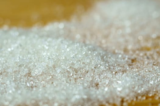 Macro spoon with sugar granules on a wooden table. Close-up of sugar crystals