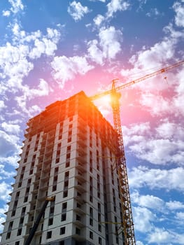 Construction crane is building a multi-storey house, in summer against the blue sky. Vertical photo