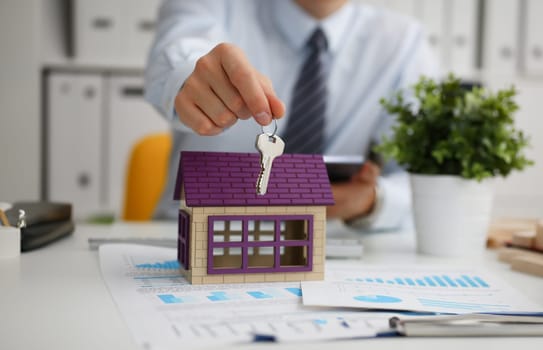 Male hand holds the key to the lock in the hand against the backdrop of the toy house. Sale purchase lease concept real estate services on the market.