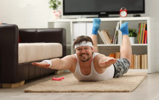 Young attractive fitness man lies on a fat mat with overweight performs exercises and smiles