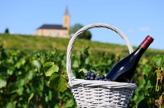 Bottle of red wine in a basket of reasons near a typical church