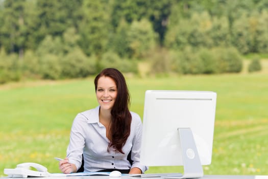 Young businesswoman in nature attractive smiling sitting behind computer table