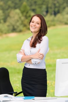 Young businesswoman in sunny nature behind table smiling crossed arms