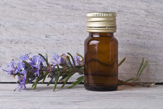 Rosemary branches and a bottle of rosemary essence on an old wooden shelf.