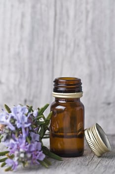 Rosemary branches and a bottle of rosemary essence on an old wooden shelf.