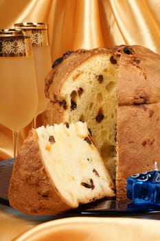 Panettone the italian Christmas fruit cake served on a blue glass plate over a yellow background and two glasses of spumante (sparkling wine). Selective focus.