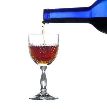 Sherry, port or whisky being poured from blue wine bottle into an elegant cut glass and isolated against white