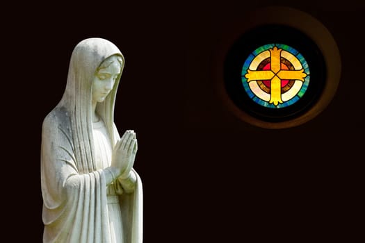Statue of Mary praying in profile with isolation path and out of focus cross shaped window on the right