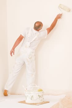 Home decorating mature man painting white wall with roller