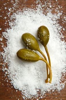 caperberries with salt close up on wood background