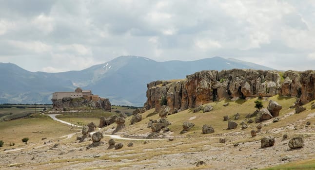 volcanic lava ash terrain with old church on a hill and mountain range in background Cappadocia , dirt tracks, cloudscape, landscape crop space and crop area