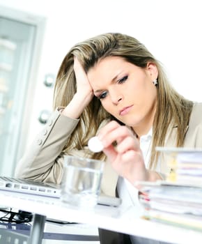 young woman stressed at work, taking an aspirin cahet