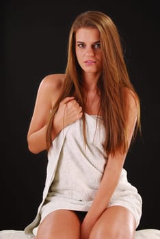 Portrait of young woman with a towel sitting on bed on dark background