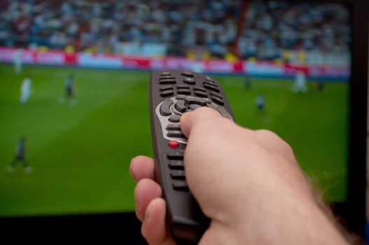 Watching TV - Man&#039 s Hand With Remote Control and TV with Football on the Screen - Shallow Depth of Field