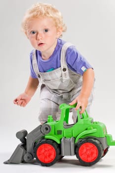 Blond handsome boy playing with green tractor