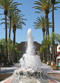 A shopping plaza with stores, flowers, and a waterf ountain for public enjoyment