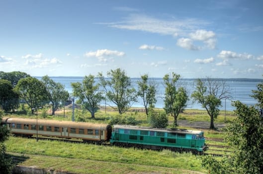 Passenger train leaving the station against the lake and blue sky